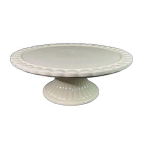 May include: Off-white ceramic cake stand with a scalloped edge and a pedestal base. The round top is smooth, and the base has vertical ribbed detailing. A classic piece for displaying baked goods.