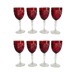 May include: Eight ruby red wine glasses with clear stems and bases. The glasses have a cut glass design on the bowl. The glasses are arranged in two rows of four.