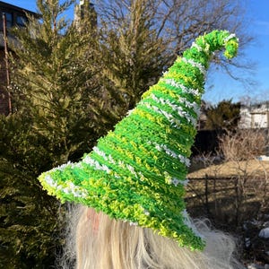 May include: A green and white striped witch hat with a curled brim. The hat is made of a fuzzy material and has a white pom-pom on top.