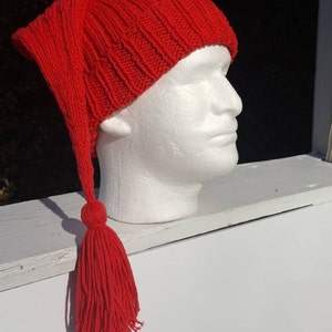 May include: Red knitted hat with a long, dangling tassel. The hat is made of a soft, warm yarn and has a ribbed texture.