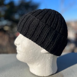 以下が含まれることがあります： リブ編み模様の黒いニット帽。白いマネキンの頭に被せられています。