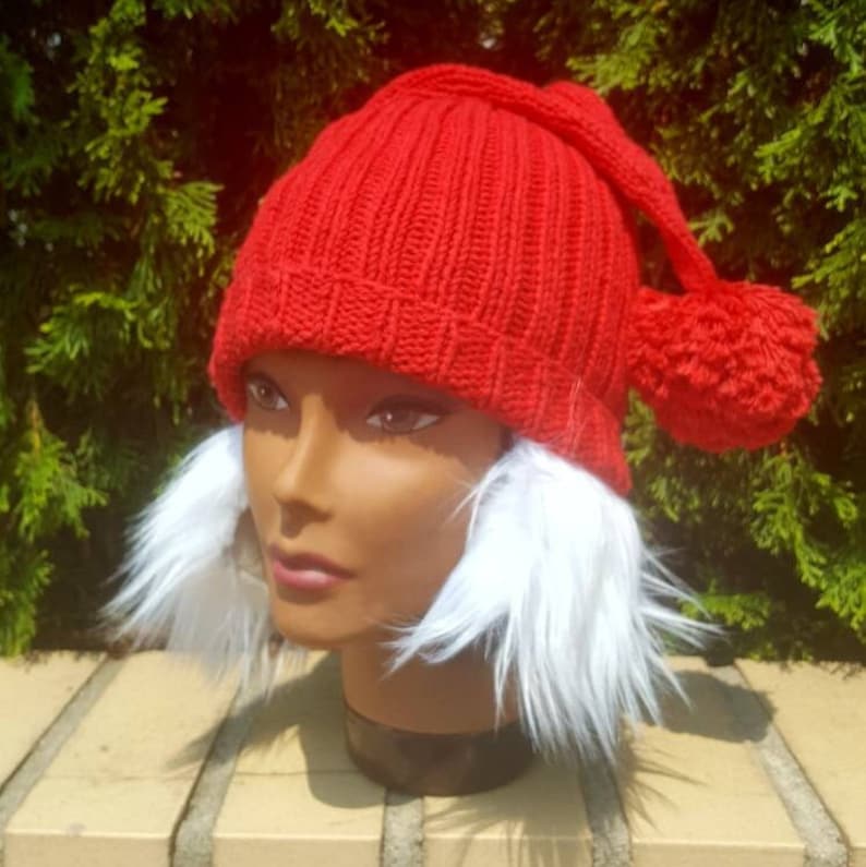 Puede incluir: Sombrero de punto rojo con un pomp&oacute;n blanco en la parte superior y orejeras de piel blanca.