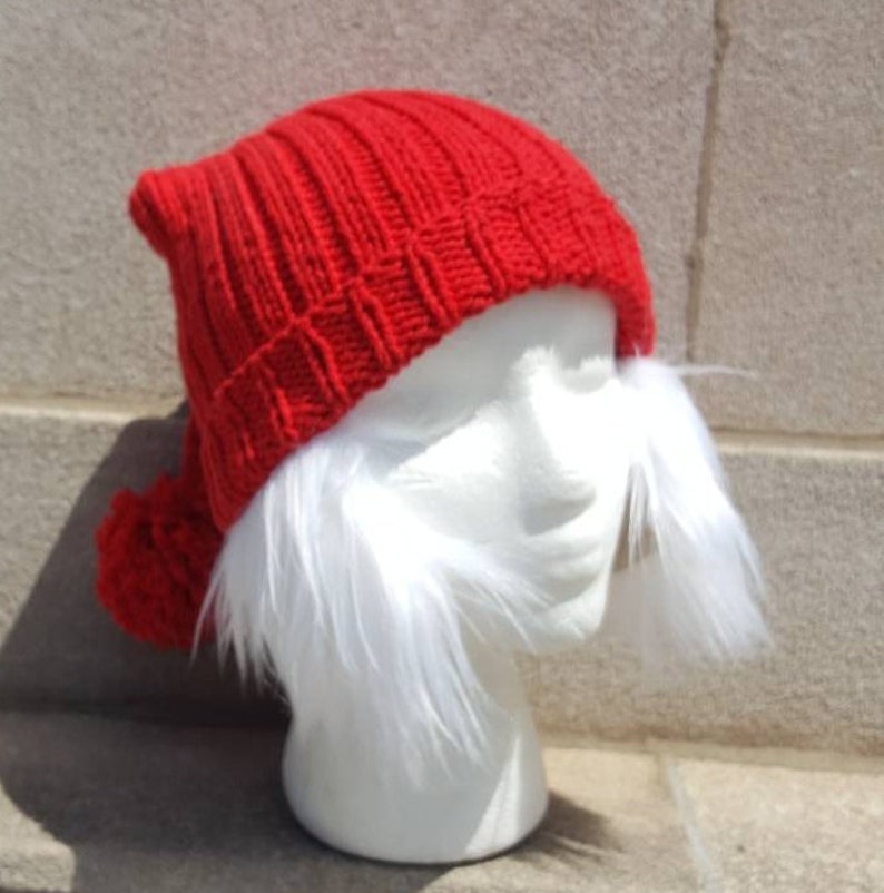 Puede incluir: Un gorro de punto rojo con un pomp&oacute;n blanco en la parte superior y un ribete de piel blanca alrededor del borde. El gorro est&aacute; en una cabeza de maniqu&iacute; blanca.