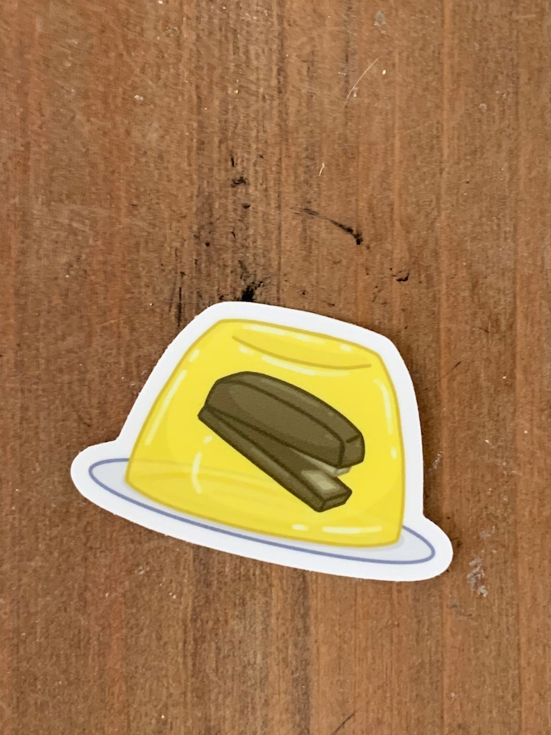 May include: A yellow jelly mold with a brown stapler inside. The mold is on a white plate.