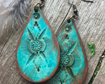 May include: Teal blue leather teardrop earrings with a distressed finish and an embossed floral design. The earrings have a hook closure.