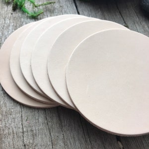 May include: A set of six off-white leather coasters. The coasters are round and have a smooth, polished surface.