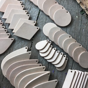 May include: Assortment of leather craft supplies in various shapes, including circles, teardrops, diamonds, and rectangles. The leather pieces are all a light beige color and have holes punched in them.