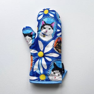 May include: Blue oven mitt with a white daisy pattern and colorful cat faces. The cats are in circular frames with a pearl border.