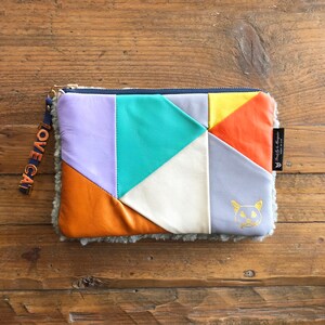 May include: A patchwork leather clutch with a fluffy gray lining. The clutch has a zipper closure and a gold metal zipper pull. The clutch is decorated with a gold cat face and the words "LOVE CAT".