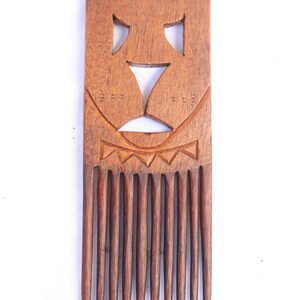 May include: A wooden comb with a carved face design. The comb has 10 teeth and is made of dark brown wood.