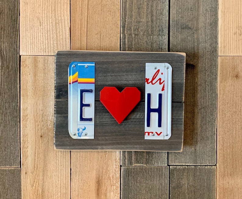 K&ouml;nnte beinhalten: Ein Holzschild mit zwei Nummernschildern, eines mit dem Buchstaben "E" und das andere mit dem Buchstaben "H". Ein rotes Herz befindet sich zwischen den Schildern. Das Schild befindet sich auf einem Holzgrund.