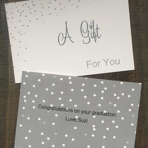 May include: A gray card with white polka dots and the text "A Gift For You" on the top half. The bottom half of the card has the text "Congratulations on your graduation. Love, Suzi."