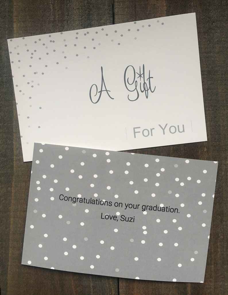 May include: A gray card with white polka dots and the text "A Gift For You" on the top half. The bottom half of the card has the text "Congratulations on your graduation. Love, Suzi."