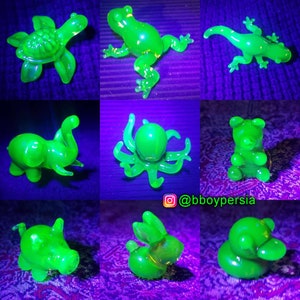 May include: Nine green glass figurines of various animals, including a turtle, frog, lizard, elephant, octopus, bear, pig, and two rabbits, all glowing under a black light.