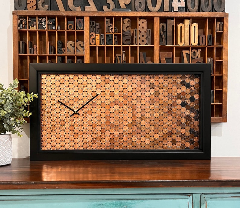 This clock has a gorgeous ombre pattern, which utilizes the patina of both new and old pennies. It simply GLOWS. And as an added bonus, it contains a hidden gem - a wheat penny. How cool is that? 
25.75" x 13.75" black frame