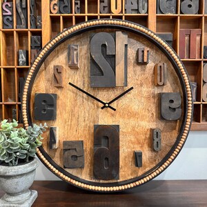 May include: A round wooden clock with a black frame and a beaded edge. The clock face is made of wood and features large wooden numbers.