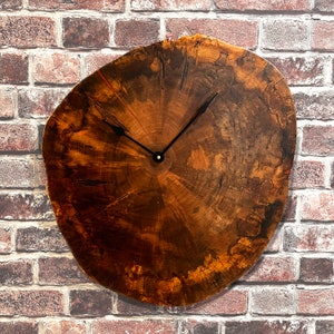 May include: A brown wood clock with black hands and a gold center. The clock is shaped like a tree trunk slice and has a natural wood grain pattern.