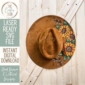 May include: A brown suede-like hat with a wide brim, adorned with hand-painted sunflowers and green leaves. The hat features the text "The Crafters Club" and "Laser Ready SVG File, Instant Digital Download, Hand Drawn & Lettered Designs."