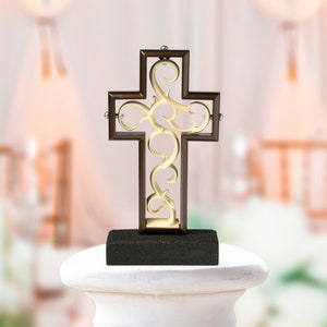 Könnte beinhalten: Ein dekoratives Holzkreuz mit einem detaillierten, komplizierten Design. Das Kreuz ist braun mit einem goldfarbenen Filigranmuster. Es wird auf einem schwarzen Sockel präsentiert.