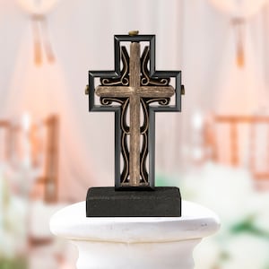 May include: A black and gold metal cross with intricate details on a black base. The cross is standing on a white pedestal.