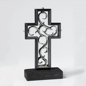 K&ouml;nnte beinhalten: Ein schwarzes Metallkreuz mit einem silbernen Filigranmuster. Das Kreuz steht auf einem schwarzen Sockel.