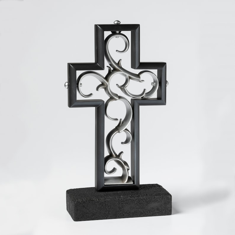 K&ouml;nnte beinhalten: Ein schwarzes Metallkreuz mit einem silbernen Filigranmuster. Das Kreuz steht auf einem schwarzen Sockel.