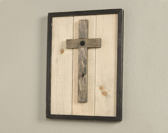 May include: A wooden cross with a black metal accent is mounted on a light wood background. The cross is framed in a black frame.