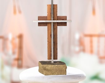 May include: A wooden cross with a silver metal accent on a gold rock base. The cross is made of two different types of wood, one light and one dark.