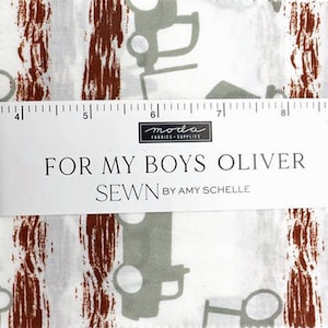 以下が含まれることがあります： グレーの乗り物と茶色の縦縞模様が繰り返される白い生地。 「FOR MY BOYS OLIVER」の文字が白いラベルに印刷され、「moda FABRICS + SUPPLIES」のロゴと「SEWN BY AMY SCHELLE」も印刷されています。