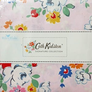 May include: A stack of fabric squares featuring a light pink background with a floral pattern of blue, yellow, orange, and pink flowers. A white paper band across the centre displays the text Riley Blake Designs and Cath Kidston Signature Collection.