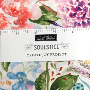 May include: Fabric with a floral design in pink, purple, and blue hues. The fabric is labeled "SOULSTICE CREATE JOY PROJECT" with a ruler along the top edge. The fabric appears to be cotton or a similar material. Measurements are in centimetres.