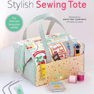 Può includere: Un'elegante borsa da cucito con un design in tessuto floreale e fruttato. La borsa presenta una cerniera, manici e finiture verde menta. Include un metro a nastro, rocchetti di filo e un taglierino rotante. Il testo recita "Stylish Sewing Tote".