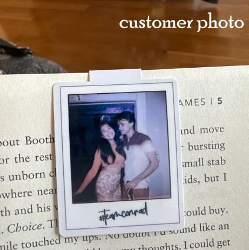 Puede incluir: Una pegatina de foto blanca de estilo Polaroid con una imagen de dos personas sonriendo a la c&aacute;mara. La foto es de una mujer con el pelo largo y oscuro que lleva un vestido marr&oacute;n y naranja y un hombre con el pelo corto y casta&ntilde;o que lleva una camisa marr&oacute;n. El texto "#teamconrad" est&aacute; escrito en negro en la parte inferior de la foto.