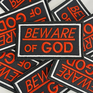 May include: A stack of black fabric patches with white and red stitching. The patches feature the text "Beware of God" in a bold, red font.