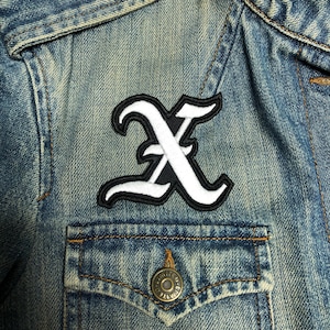 May include: A white letter X patch with black outlines, sewn onto a blue denim jacket.