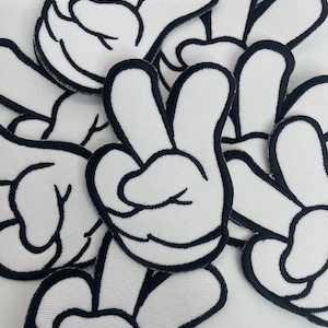 May include: A pile of white fabric patches with black outlines, shaped like a hand giving the peace sign.