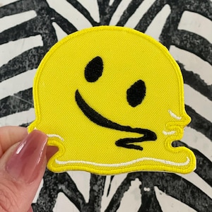 May include: Yellow smiley face patch with a black outline and a dripping effect. The patch is made of fabric and has a white border.