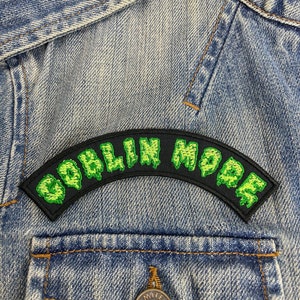 May include: Green and black embroidered patch with the text "Goblin Mode" on a denim jacket.