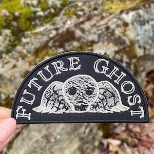 May include: A black and white embroidered patch with the text "FUTURE GHOST" in a semi-circle around a skull with wings.