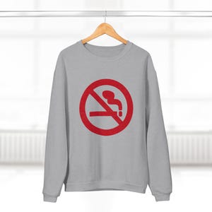 K&ouml;nnte beinhalten: Ein graues Sweatshirt mit einem roten Rauchverbotsschild auf der Vorderseite. Das Schild hat einen diagonalen Strich durch eine Zigarette mit Rauch, der aus ihr aufsteigt.