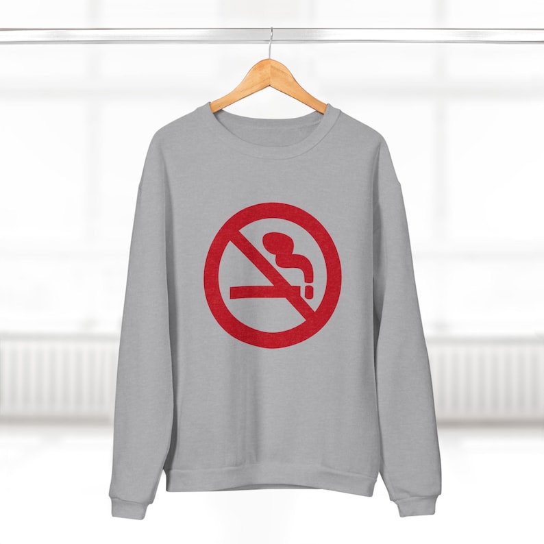 K&ouml;nnte beinhalten: Ein graues Sweatshirt mit einem roten Rauchverbotsschild auf der Vorderseite. Das Schild hat einen diagonalen Strich durch eine Zigarette mit Rauch, der aus ihr aufsteigt.