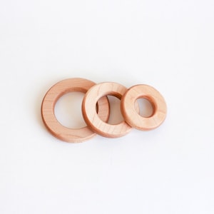 May include: Three wooden rings of different sizes, nested together. The rings are made of light brown wood and have a smooth, polished finish.