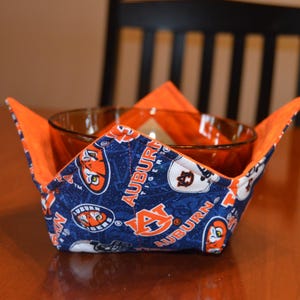 May include: A blue and orange fabric bowl cozy with the words "Auburn Tiger" and "Auburn" printed on it. The cozy is holding a clear glass bowl.