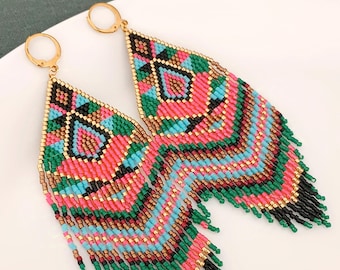 Puede incluir: Un par de pendientes largos de cuentas de colores con un patrón geométrico. Los pendientes están hechos con cuentas de color rosa, azul, verde, dorado y negro. Los pendientes cuelgan de ganchos dorados.