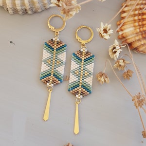 May include: A pair of gold beaded earrings with a geometric pattern in shades of blue, green, white, and brown. The earrings have a long, thin gold dangle.
