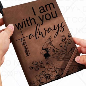 May include: Brown journal with the text "I am with you always" and "Matthew 28:20". The journal features a detailed illustration of a cardinal bird and floral elements.
