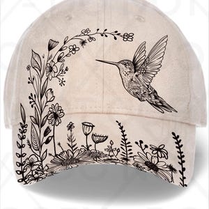 May include: A beige baseball cap with a black and white floral and hummingbird design. The cap has a curved peak and a rounded crown, suitable for outdoor wear. The design includes flowers and foliage.