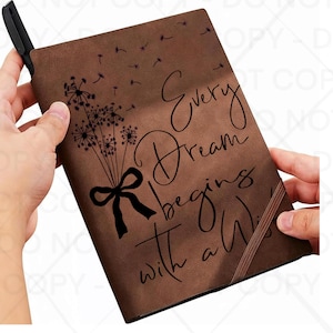May include: A brown notebook with the quote "Every Dream begins with a Wish" in a cursive font. The notebook features a dandelion design with a black bow. A black pen is inserted into the spine.