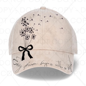 Puede incluir: Gorra de béisbol beige con un diseño de diente de león negro y el texto "Every dream begins with a wish". La gorra tiene una visera curva y una corona redonda. El diseño del diente de león incluye un lazo.
