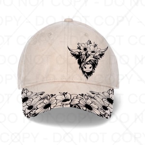 May include: A beige baseball cap featuring a black graphic of a Highland cow head adorned with flowers on the front panel and a black floral pattern printed across the entire brim, creating a contrast against the light-coloured fabric of the hat.
